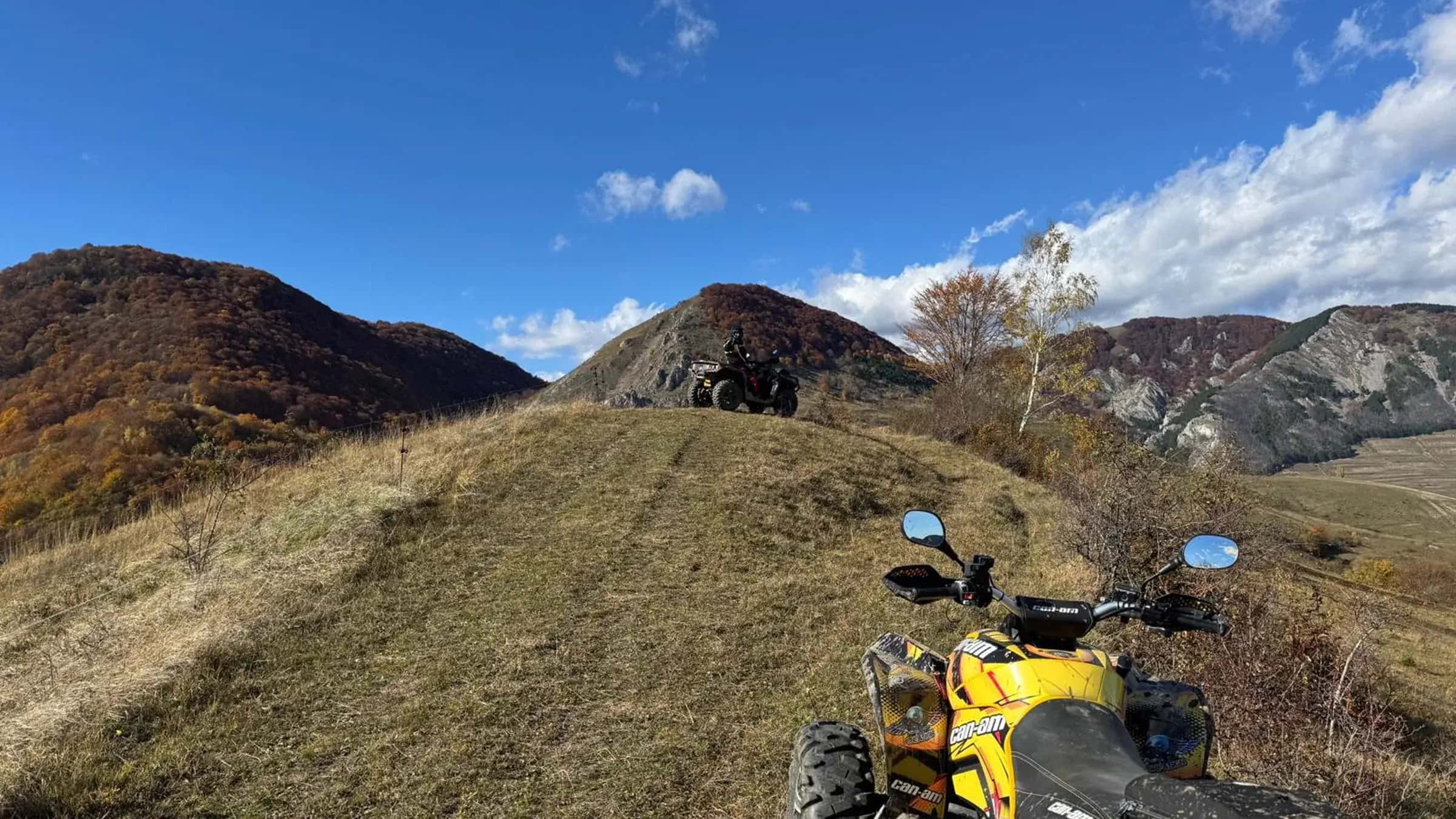 Two ATVs on a grassy saddle with dramatic rocky peaks behind
