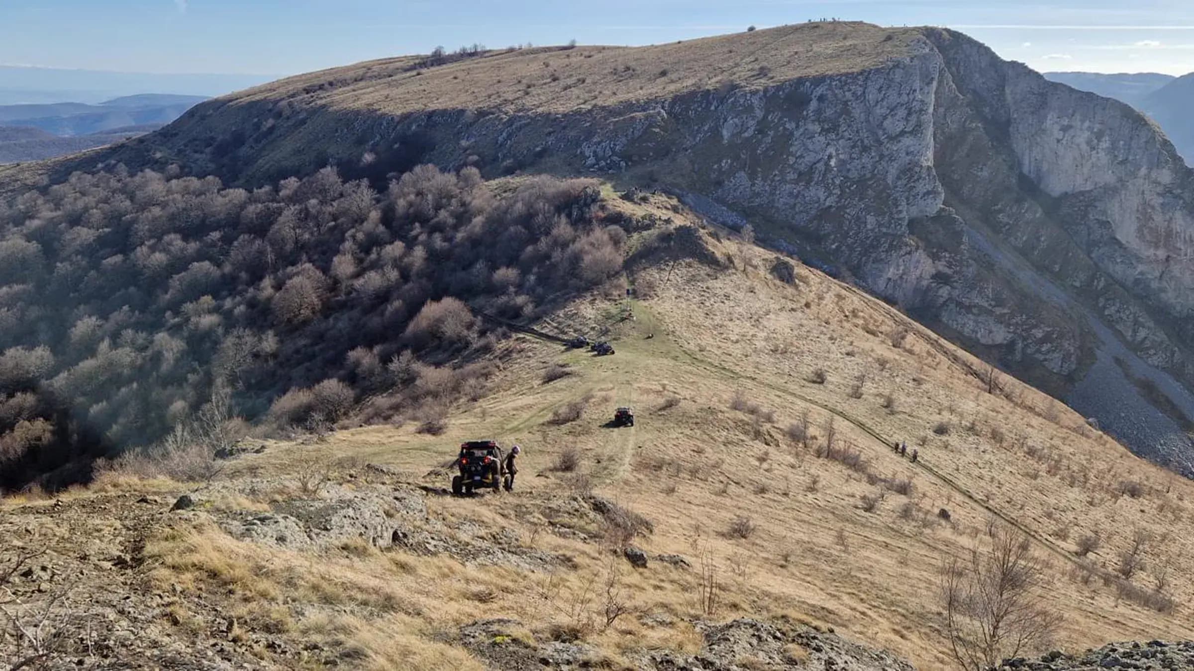 A dramatic rocky cliff escarpment with machines on the ridge trail
