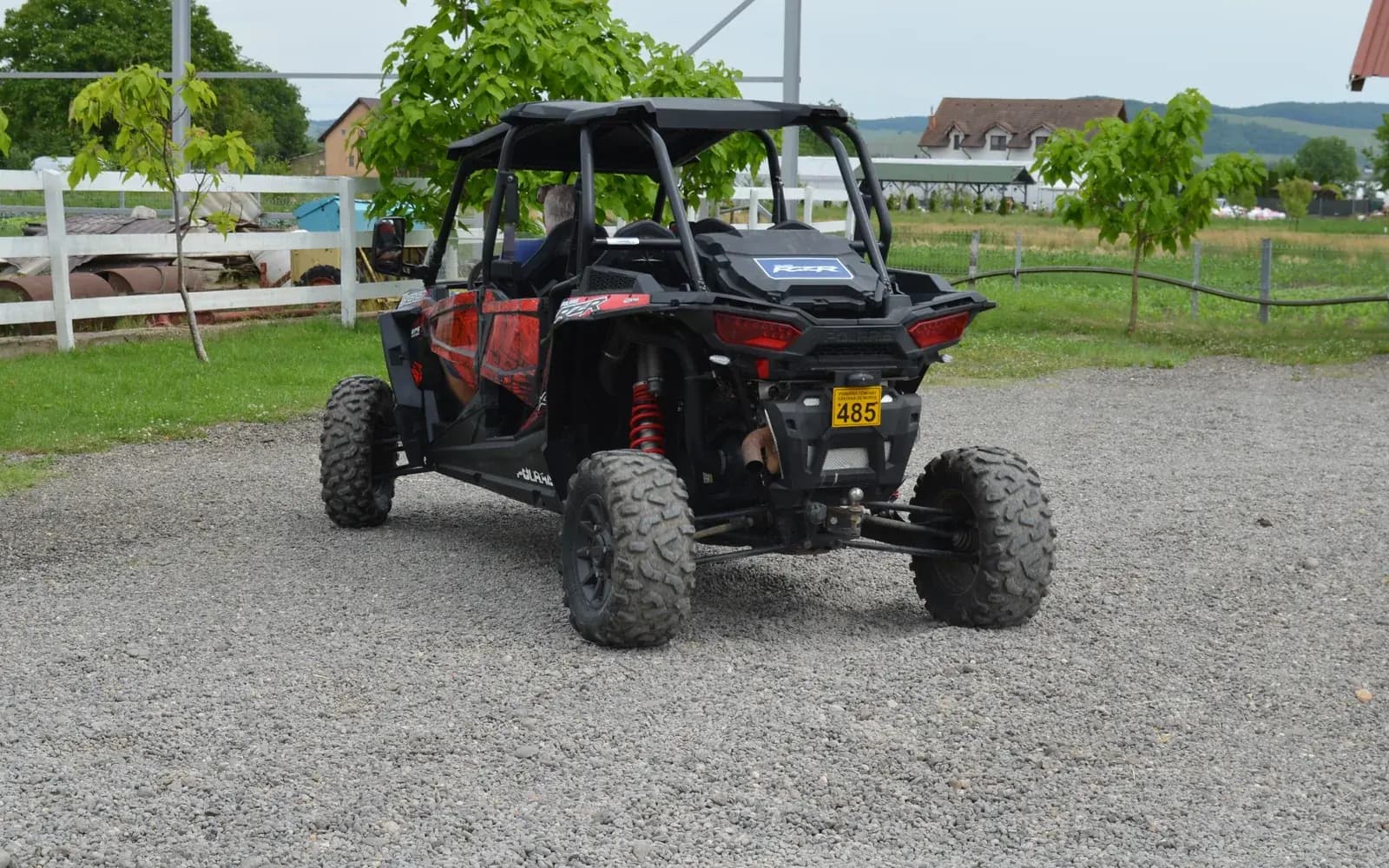 A four-seat Polaris RZR parked in the farm's gravel yard, white paddock fencing and hills behind