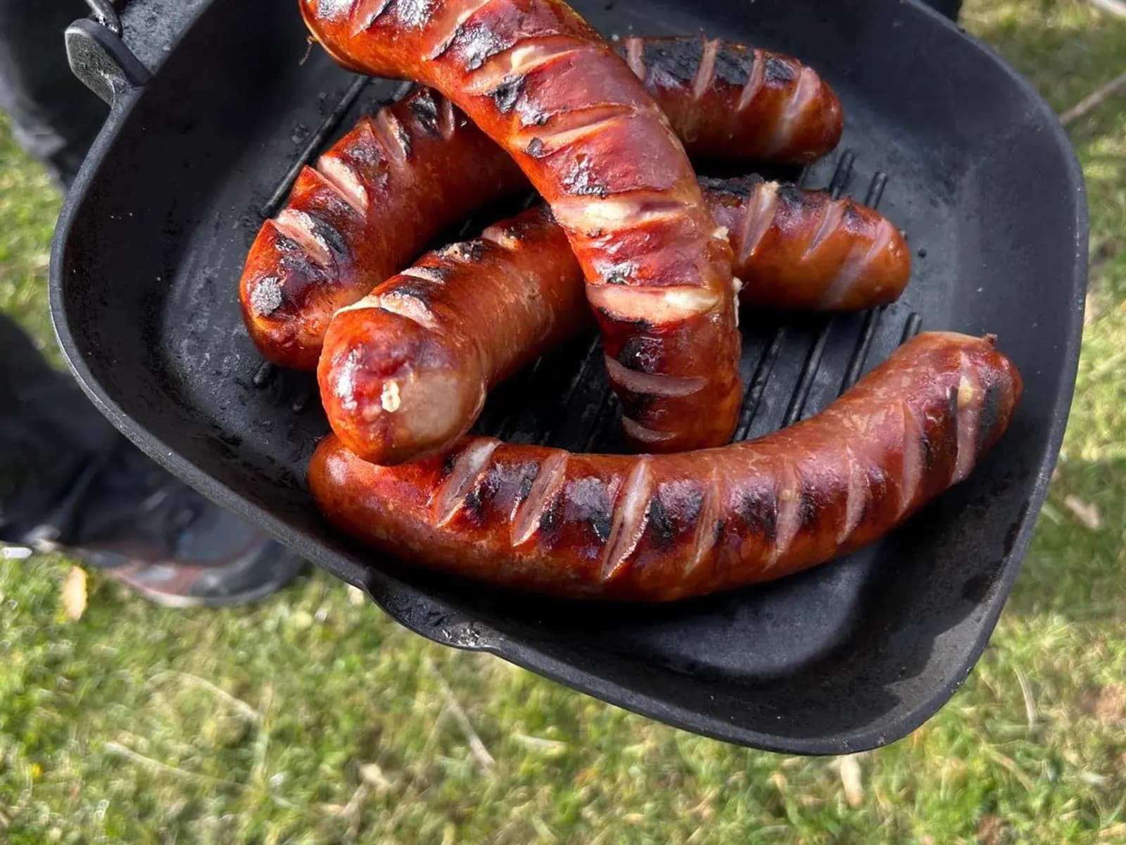 Sausages grilling on a cast-iron pan over an open fire