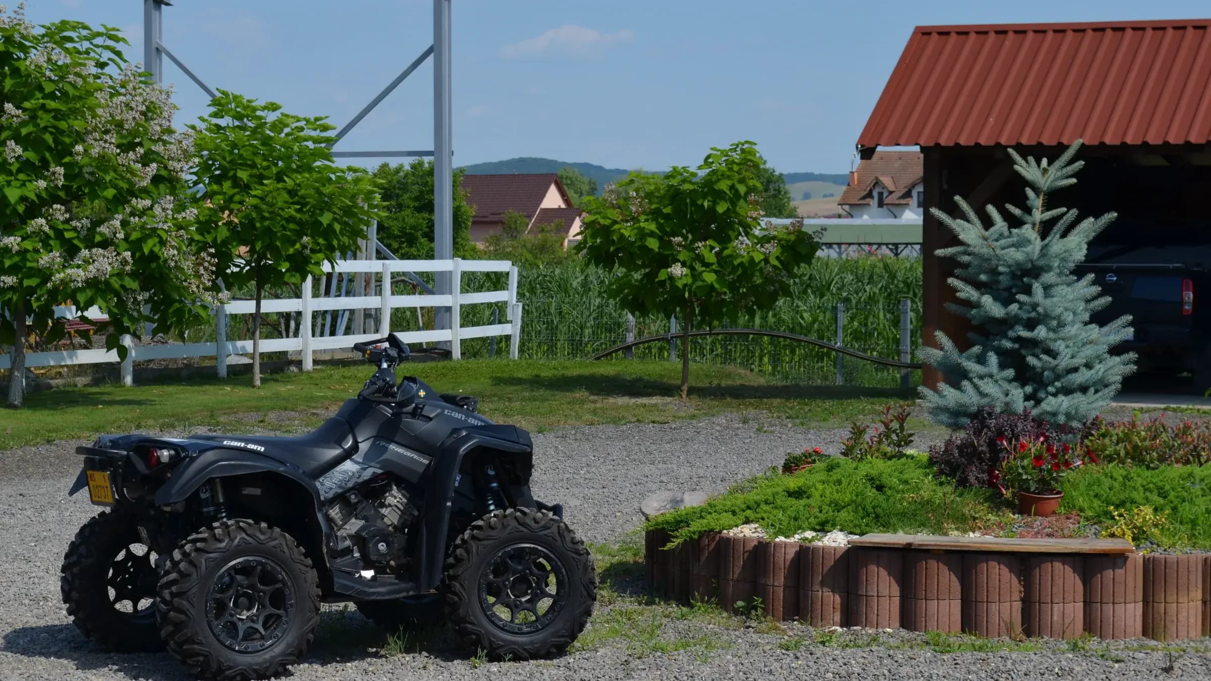 An ATV parked in the farmyard beside a white fence and the farmhouse
