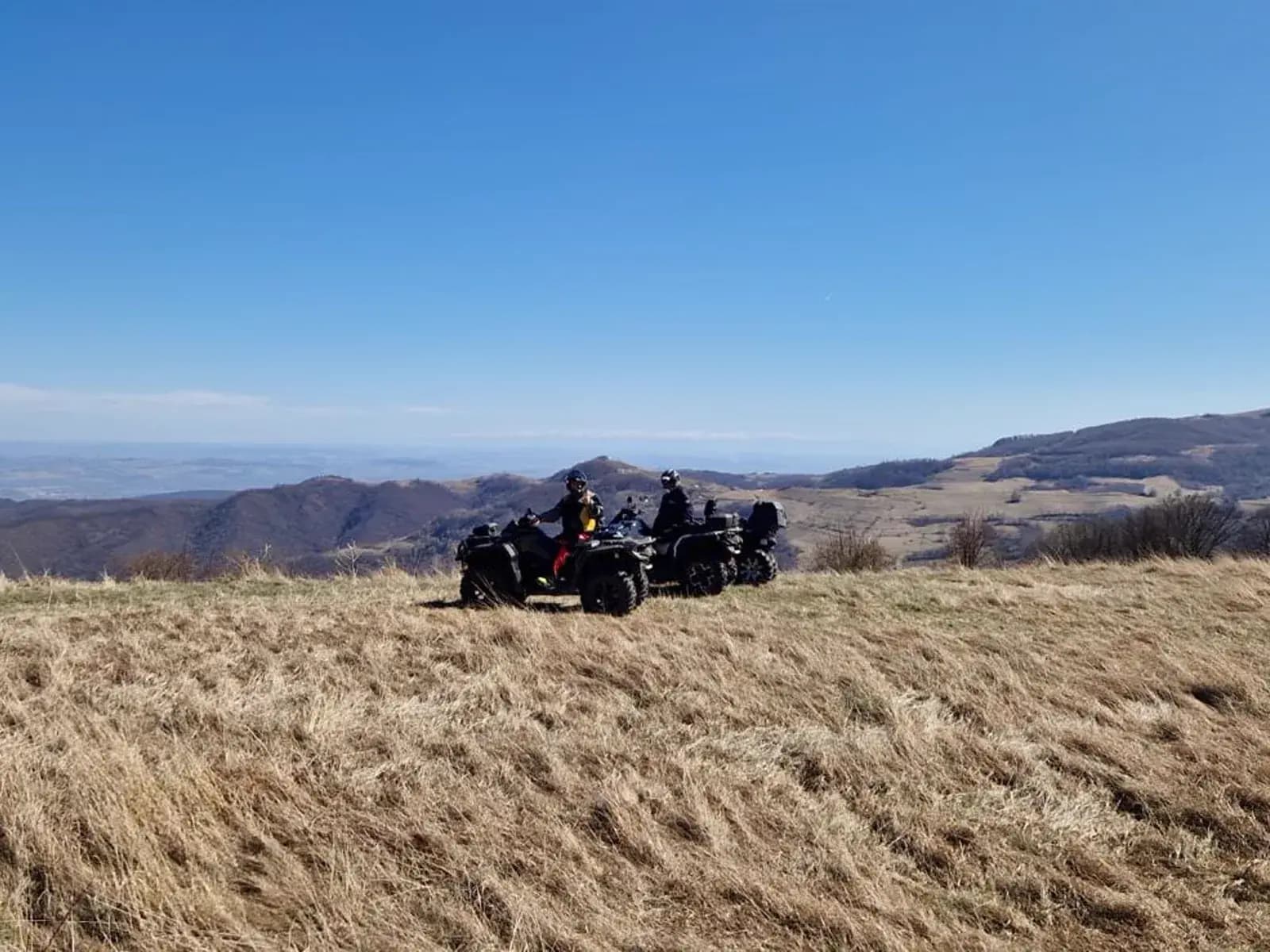 Two ATVs on a dry grass ridge with a distant hazy mountain