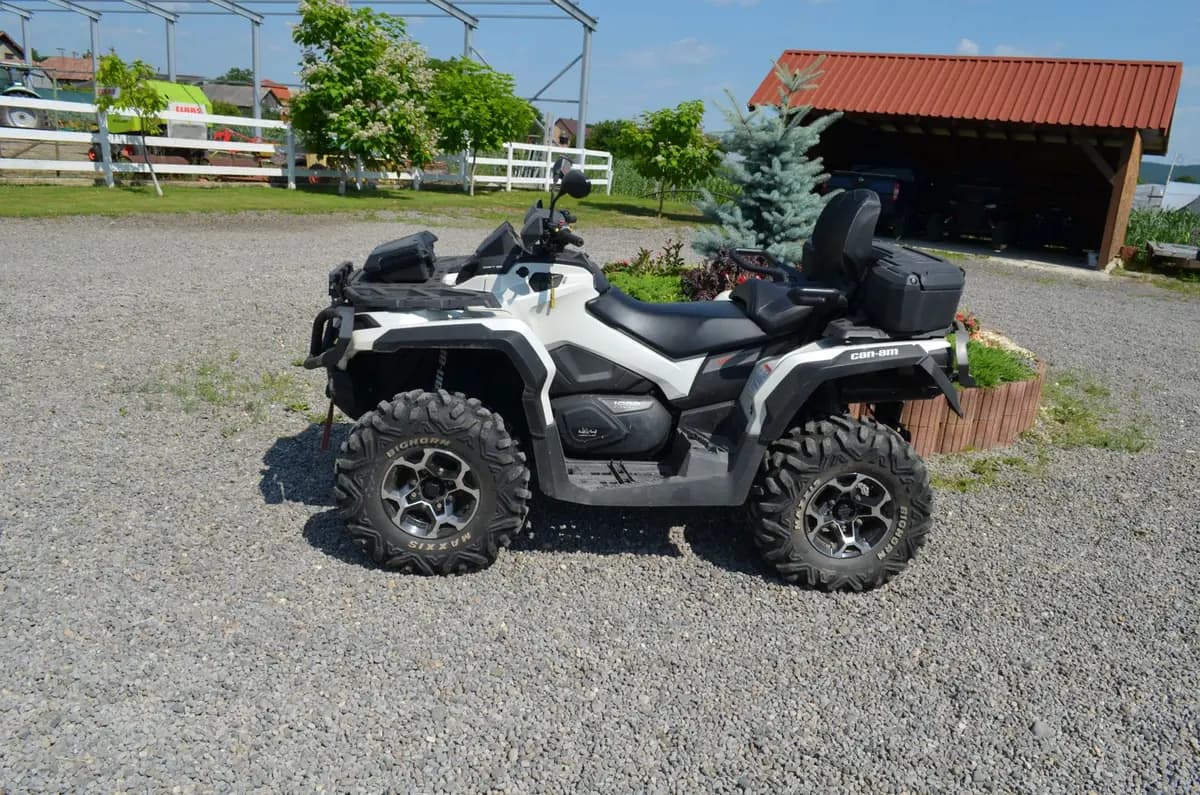 A white Can-Am Outlander 1000 quad with a two-up seat and rear luggage box, parked on the farm's gravel yard