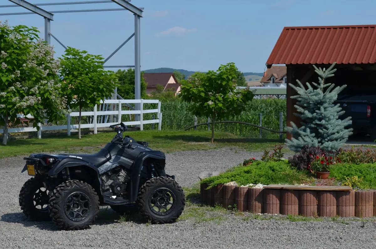 A black Can-Am Renegade sport quad parked on gravel in front of the farm's white paddock fence