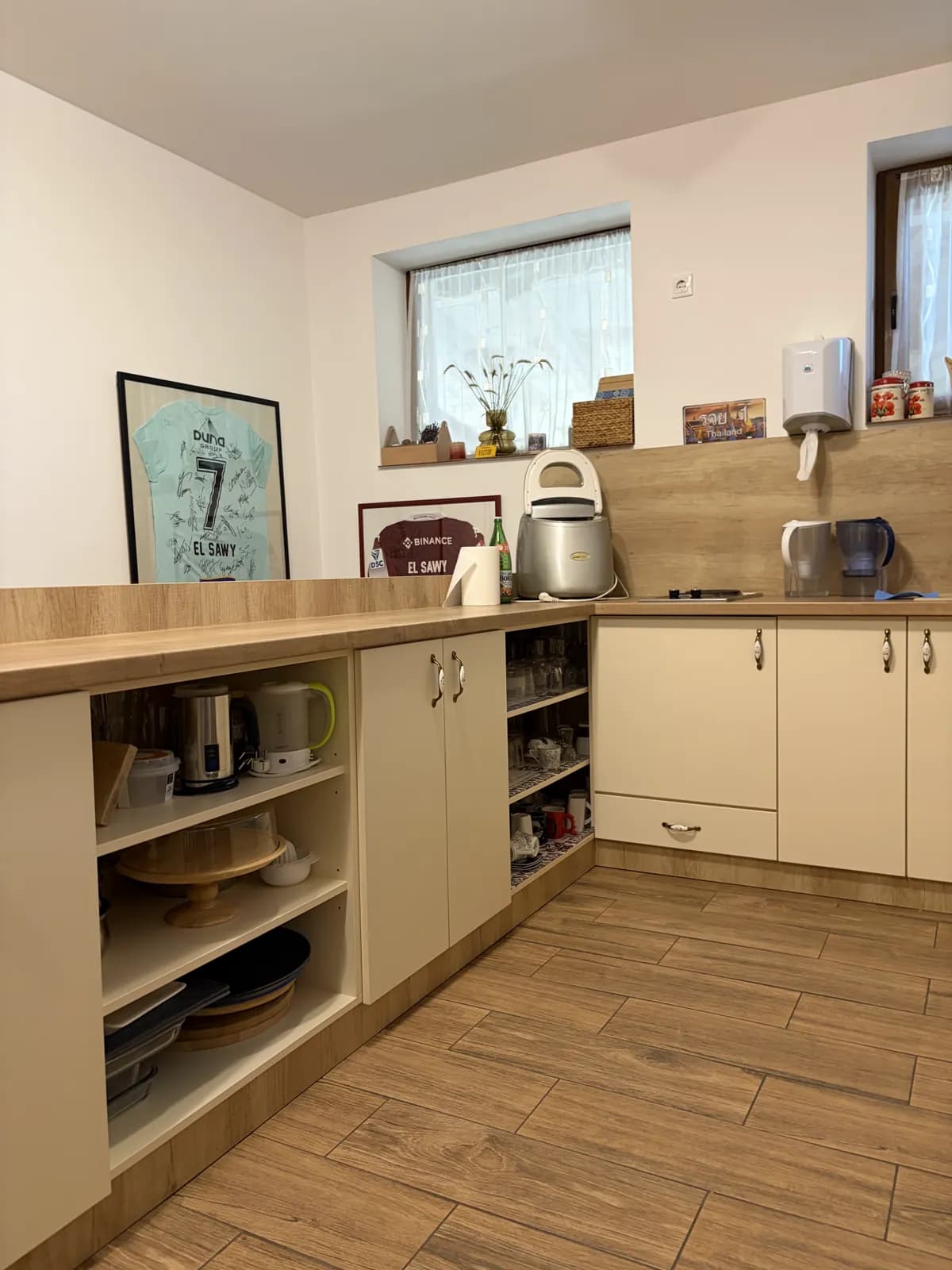 L-shaped cream kitchen cabinets with a wooden worktop, open shelves of kettles and tableware, and a hob under the window