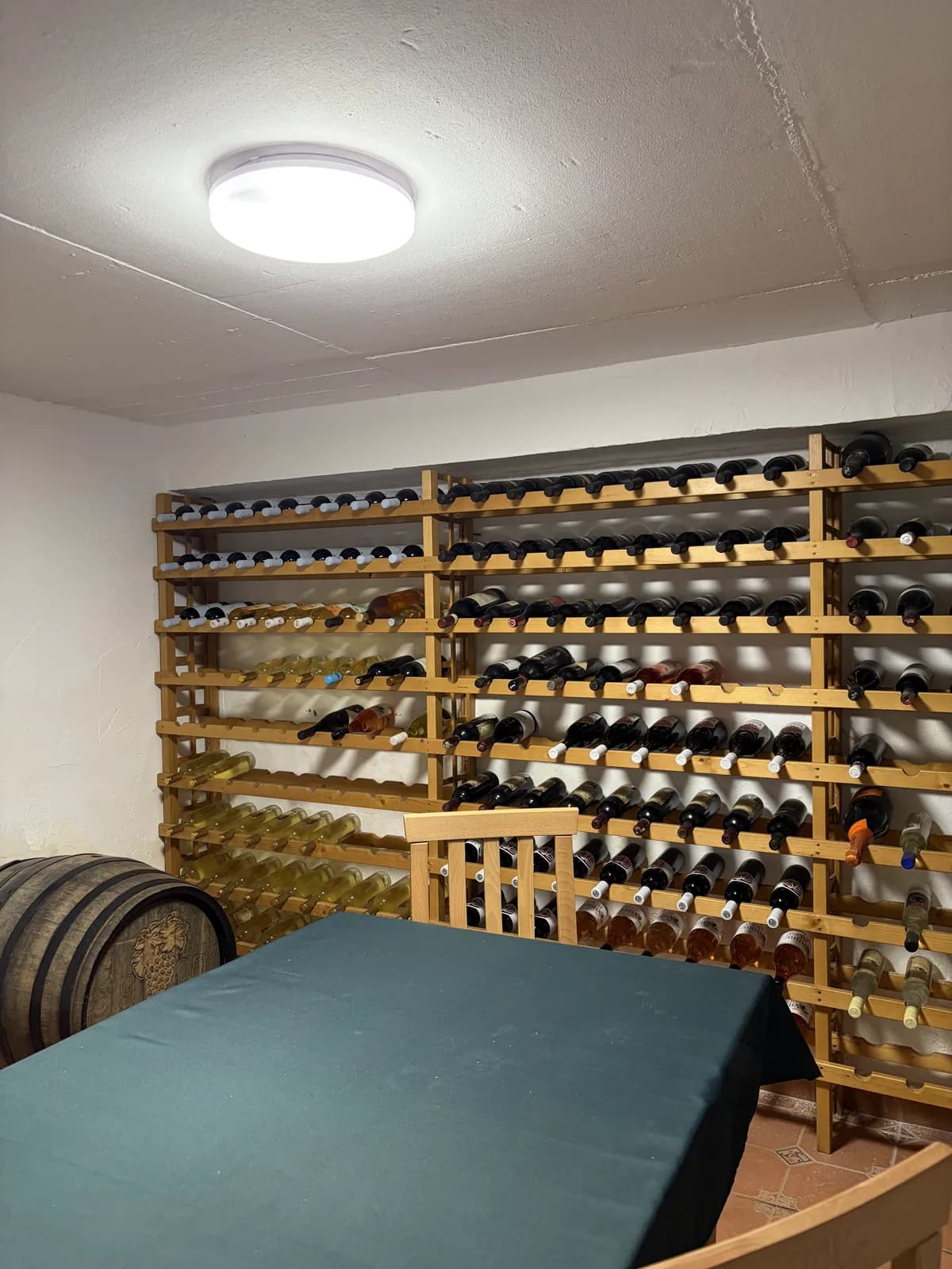 A wall of racked wine bottles beside an oak barrel and a table in a small cellar room