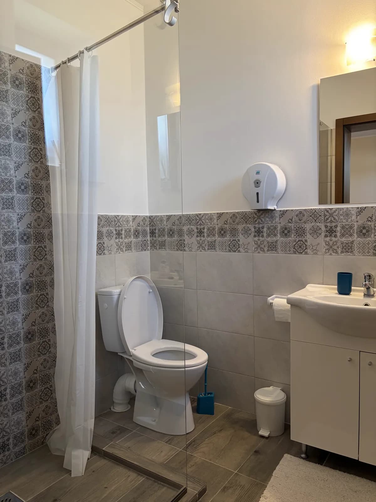 An ensuite bathroom with blue patterned tile, a curtained shower, toilet and sink