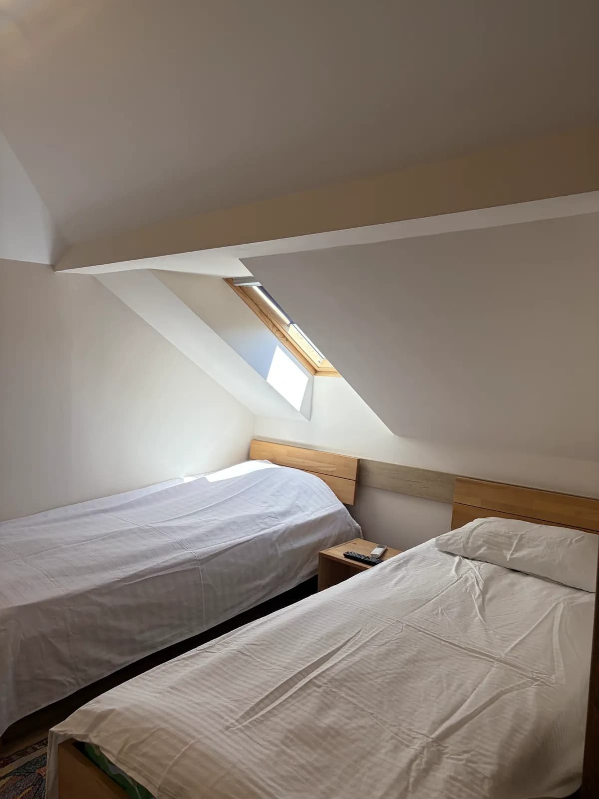 An attic room with a sloped ceiling and a skylight above two made single beds