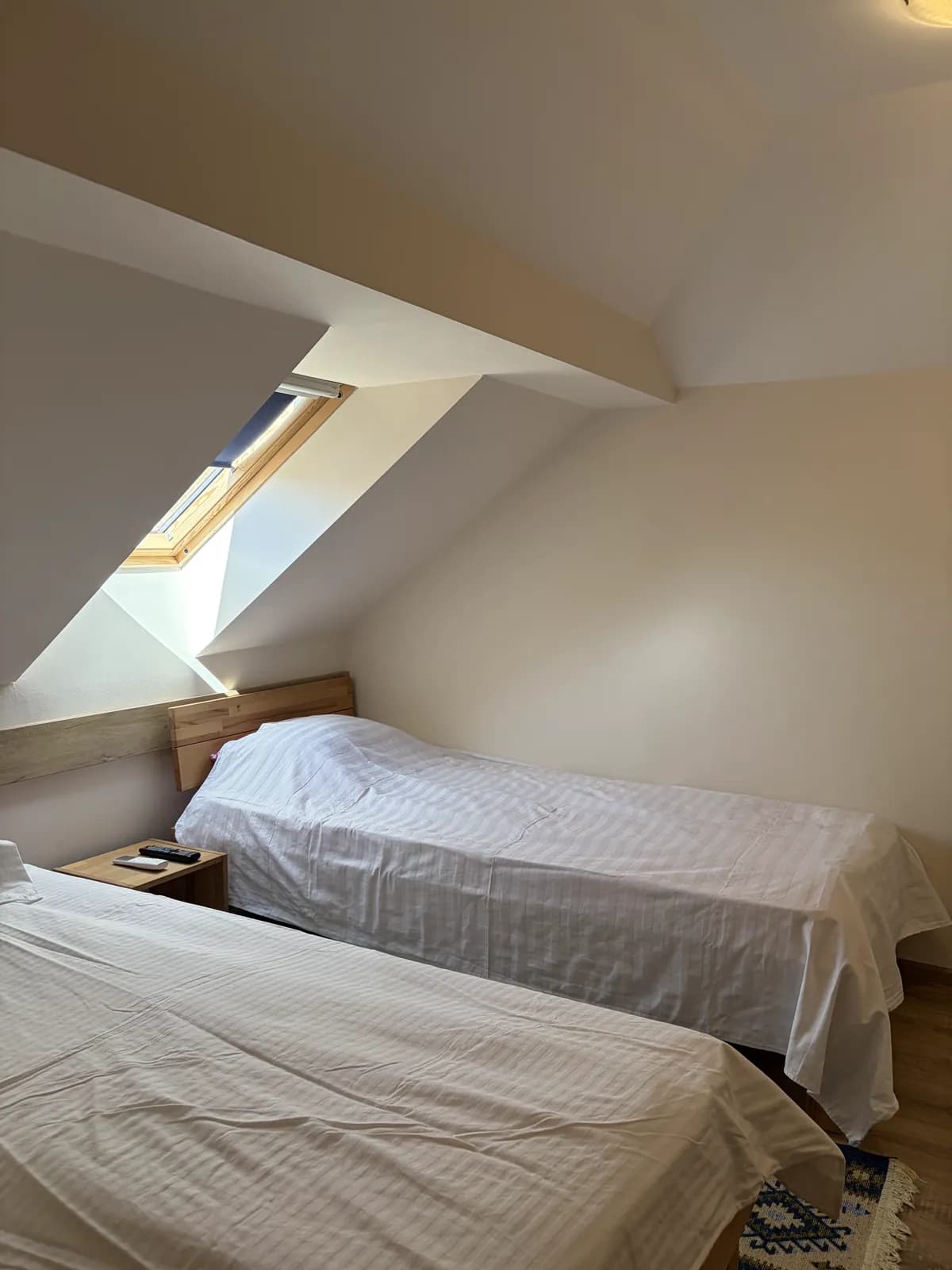 An attic room with two made single beds side by side beneath a skylight in the sloped ceiling