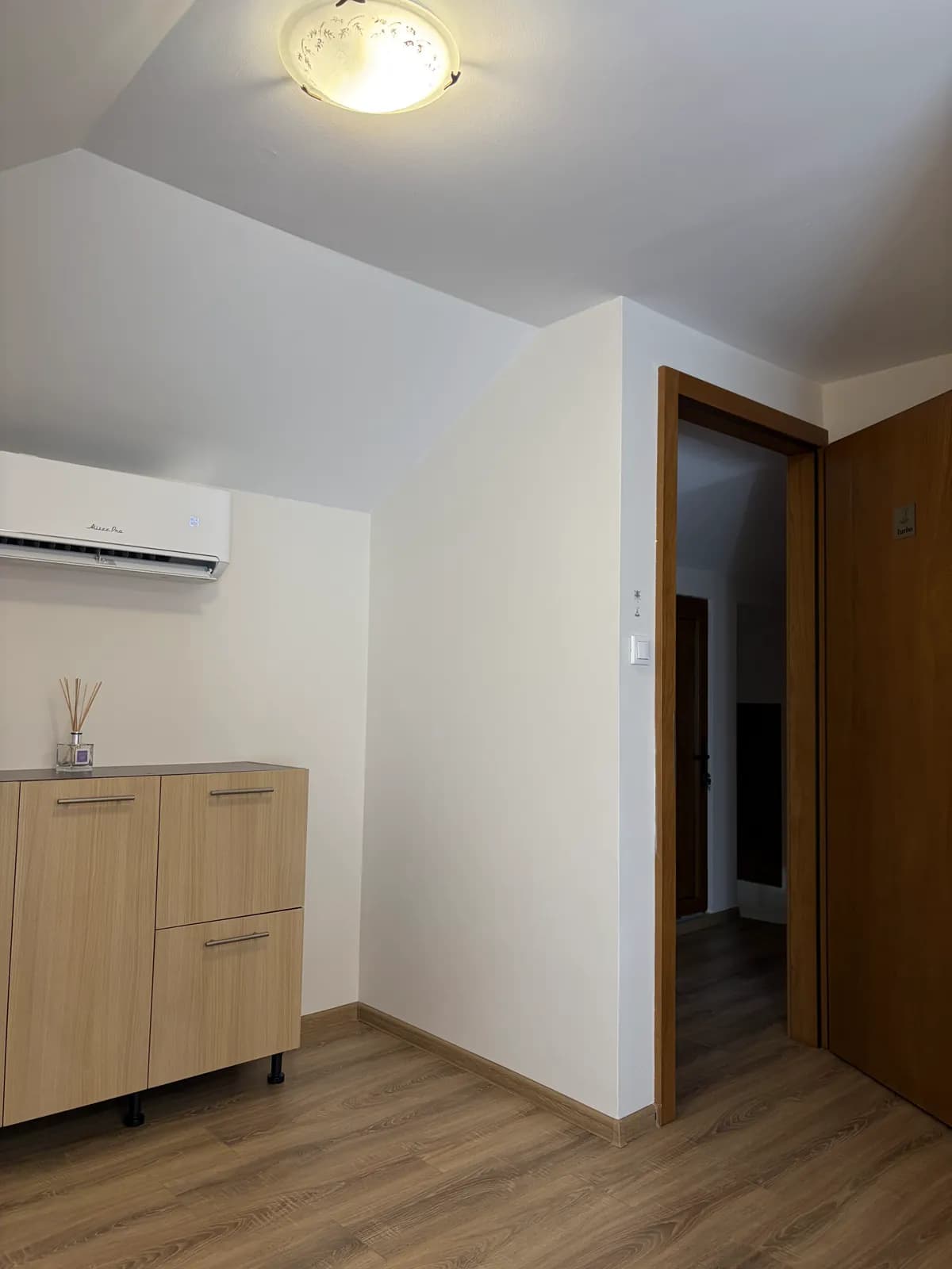 The same attic room's other wall, with an air conditioning unit, a low wooden cabinet and the open door to the corridor