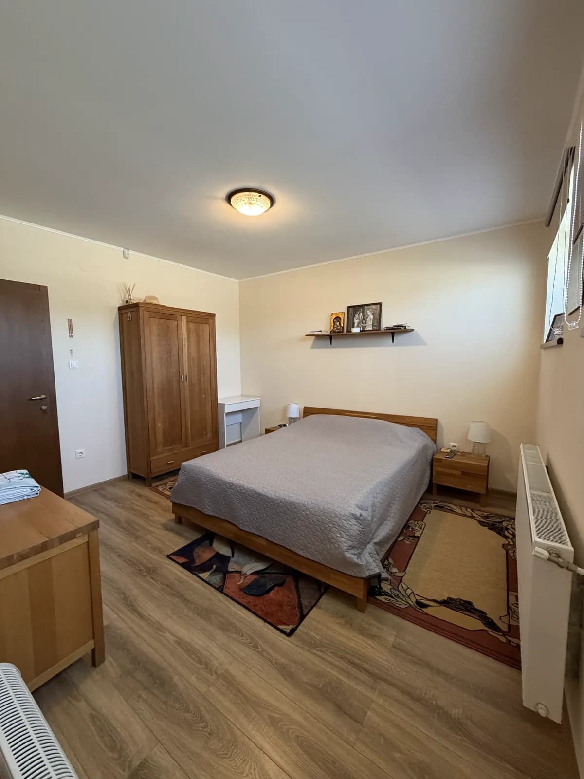A ground-floor double room with a made bed, an oak wardrobe and a wall shelf holding a small icon and a framed print