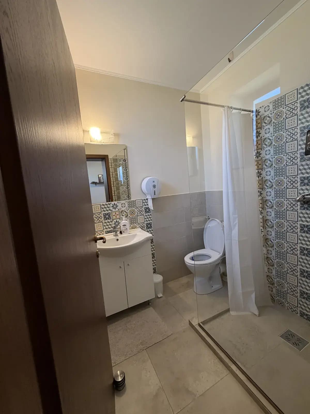 An ensuite bathroom with patterned mosaic tile, a corner shower, toilet and sink