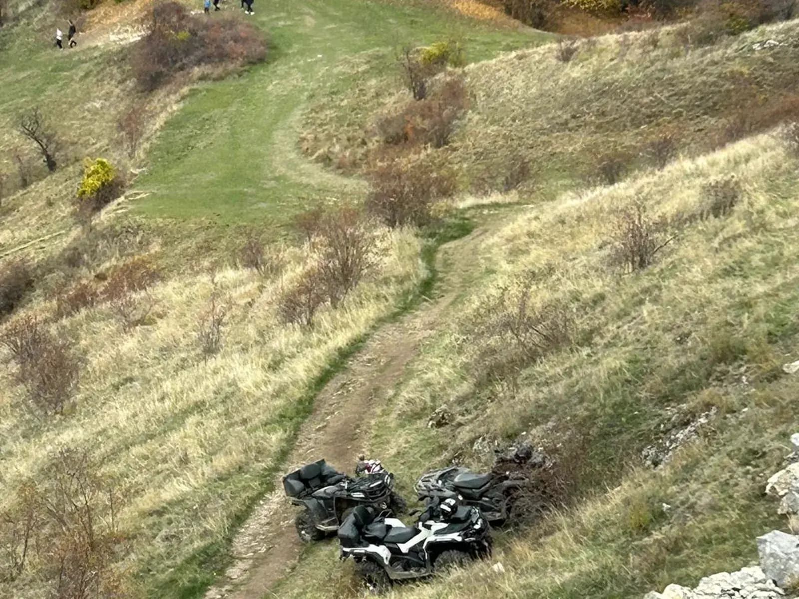 An aerial view down a grassy ravine at three parked ATVs