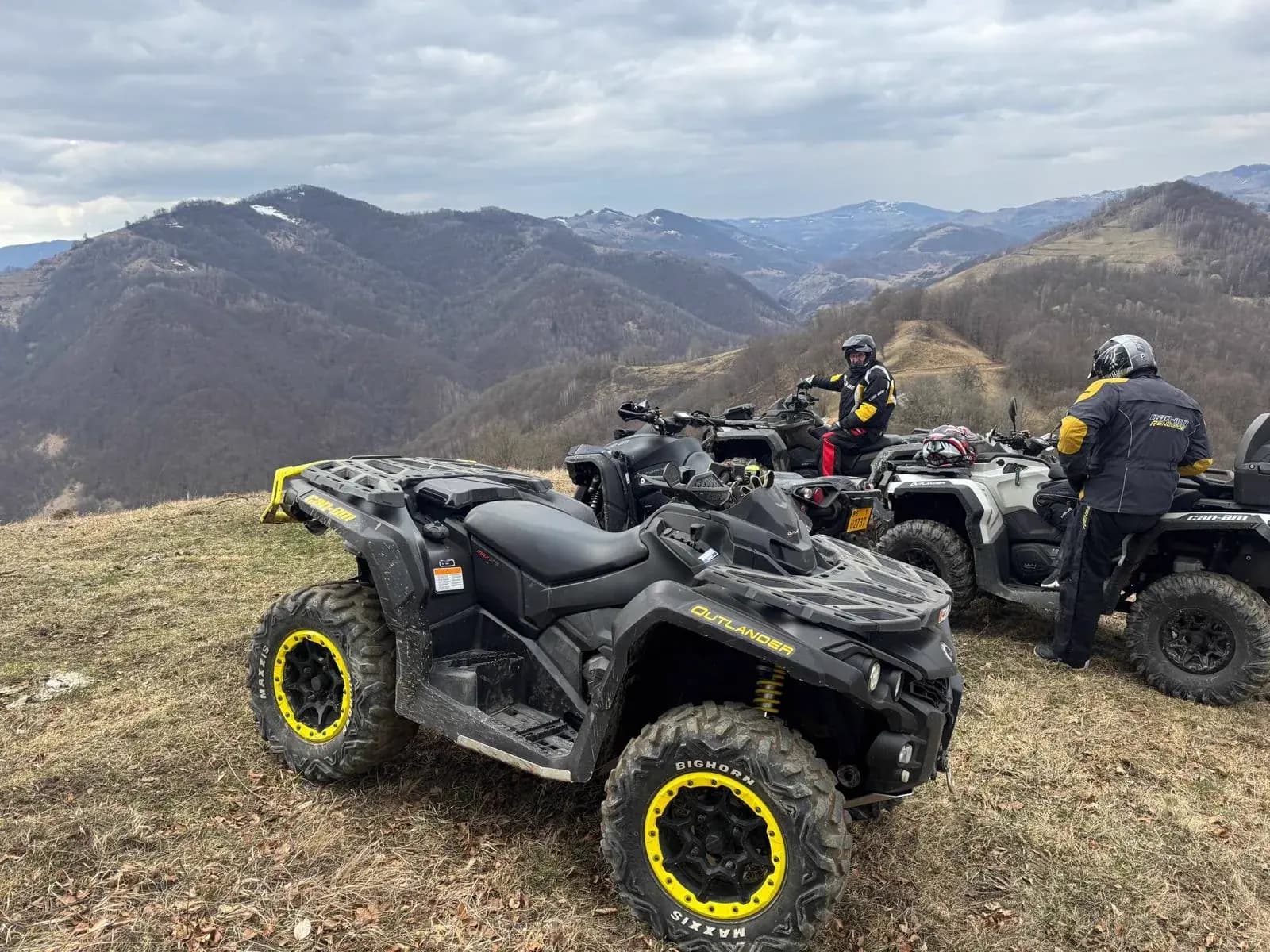 ATVs on a ridge under a dramatic overcast sky with distant peaks