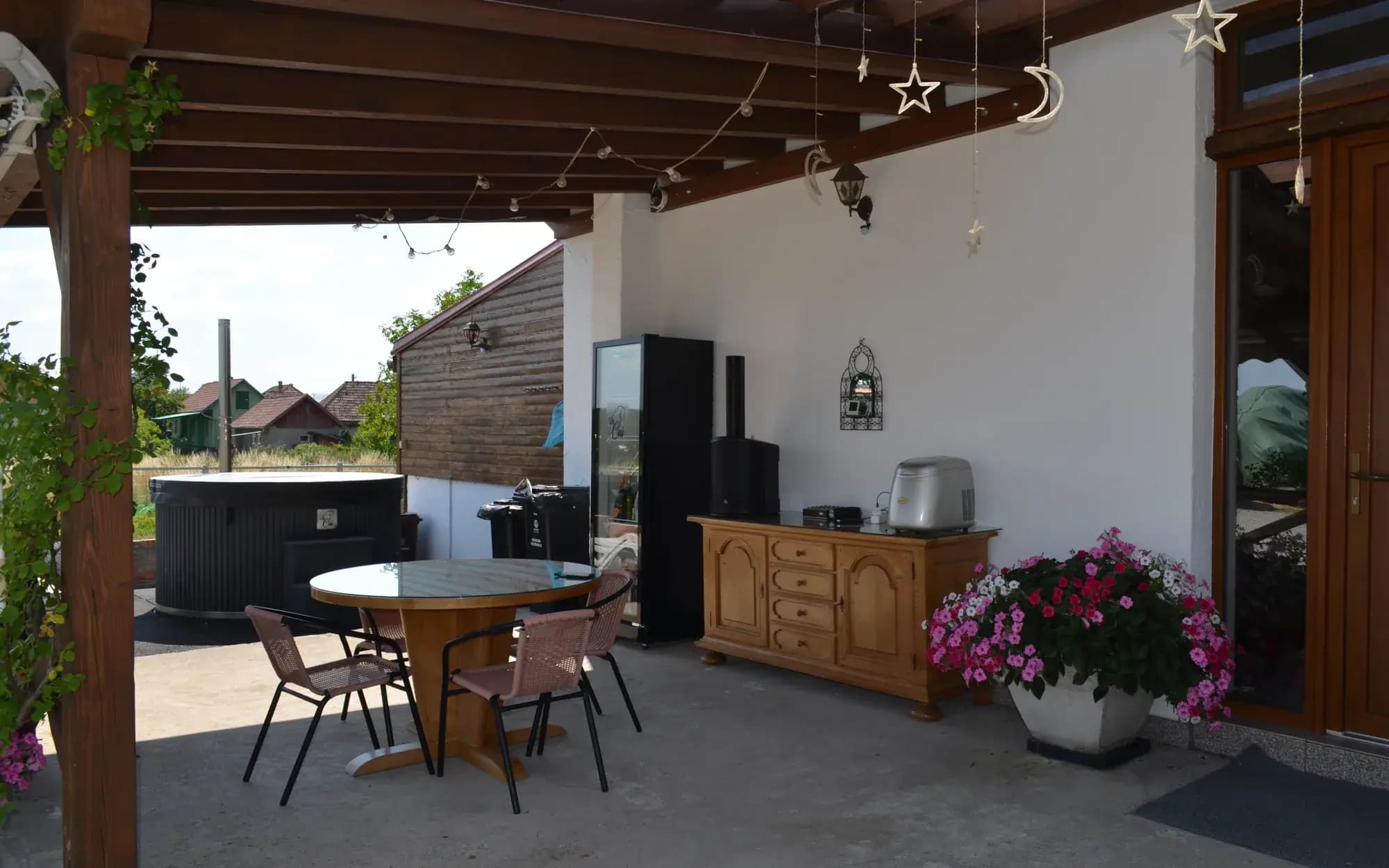 A covered patio with a round table, log store and firewood-heated hot tub, roses climbing the timber posts